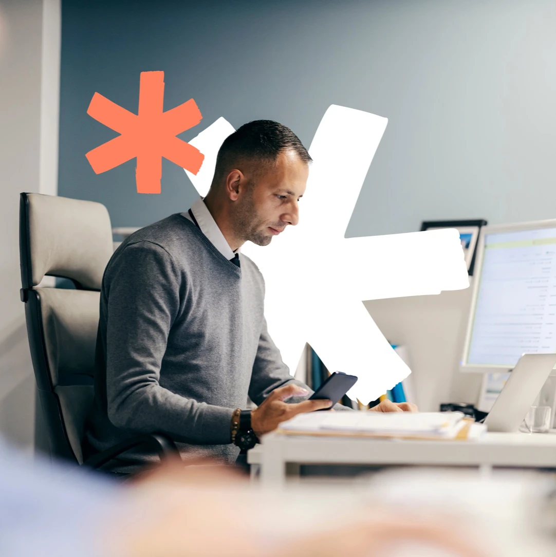 Mann mit Smartphone in der Hand schaut auf sein Notebook